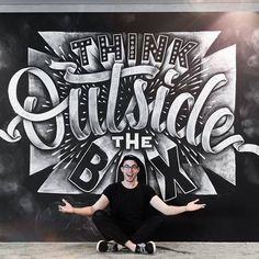 a man sitting on the ground in front of a black and white wall with lettering