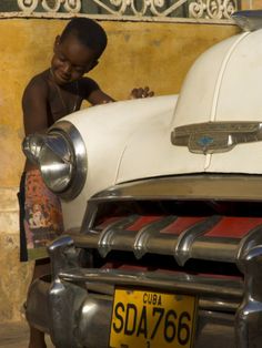 a young boy is working on the hood of an old car in havana, cuba