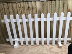 a white picket fence sitting in front of a wooden fence next to a black dog