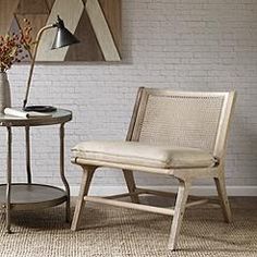 a chair next to a table with a lamp and vase on it in front of a white brick wall