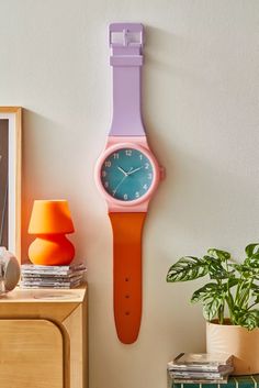 a pink and blue watch hanging on the wall next to a potted green plant