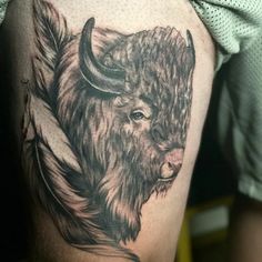 a black and white bison tattoo on the side of a man's thigh,