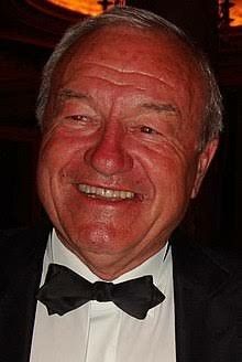 an older man in a tuxedo smiles at the camera