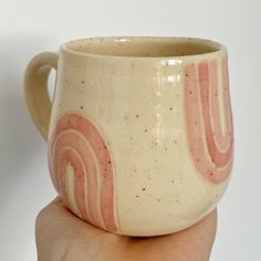 a hand holding a coffee cup with pink swirls on it's side and white background