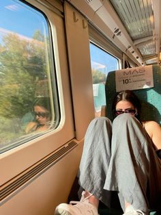 a woman sitting on a train seat with her feet up against the wall and looking out the window