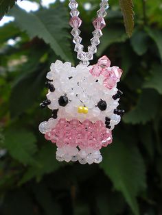 a hello kitty necklace is hanging from a tree with green leaves in the back ground