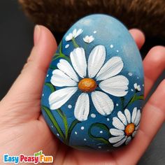 a hand holding a painted rock with daisies on it