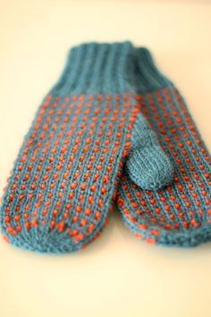 two blue and orange knitted mittens sitting on top of a white countertop