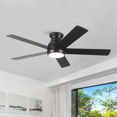 a black ceiling fan in a white room with large windows and pictures on the wall