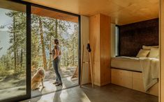 a woman standing next to a dog in front of a sliding glass door looking out onto the woods