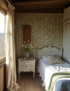 two beds in a room with floral wallpaper and curtains on the window sill