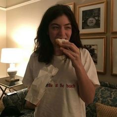 a woman eating a donut in front of a living room table with pictures on the wall