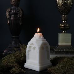 a white candle sitting on top of a table next to two vases filled with moss