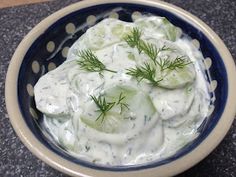 a bowl filled with cucumbers and sauce on top of a granite countertop