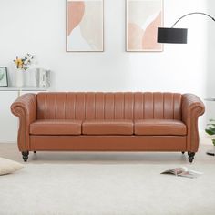 a brown leather couch sitting in a living room next to a white rug and two pictures on the wall