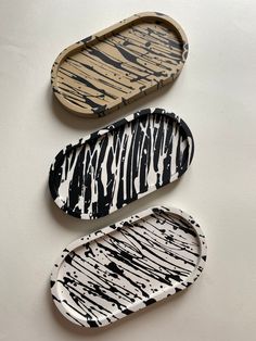 three wooden trays with black and white designs on them, one is shaped like an oval