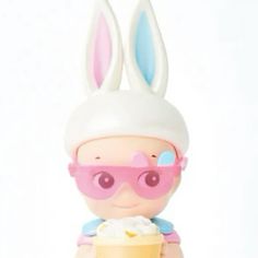 a toy doll with sunglasses and bunny ears holding a cup filled with whipped cream in front of a white background