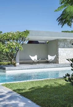 two lawn chairs sitting next to a swimming pool in the middle of a lush green yard