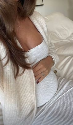 a woman sitting on top of a bed wearing a white sweater and silver bracelets