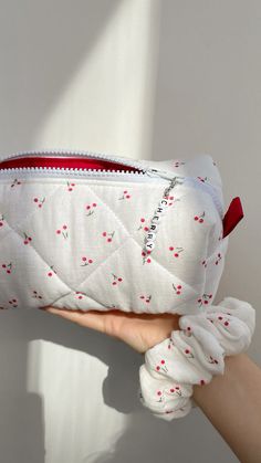 a hand holding a white purse with red flowers on it and the zipper is open