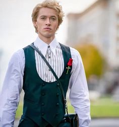 a young man in a green vest and white shirt with a red rose on his lapel