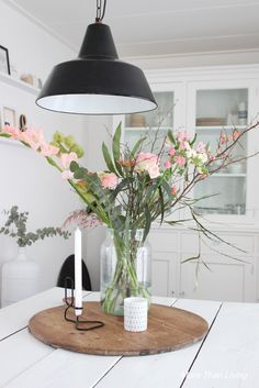 a table with flowers in vases on top of it and a light hanging from the ceiling