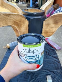 a person holding a can of paint in front of a wooden bench with other furniture