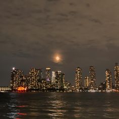 the city skyline is lit up at night, with bright lights reflecting off the water