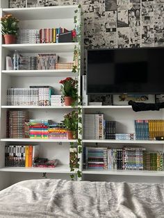 a book shelf filled with books next to a tv on top of a white bed