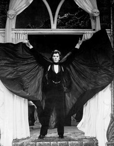 a woman standing in front of a window with her arms spread wide and wearing a black dress