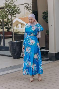 The Leena satin maxi dress from Annah Hariri is a stunning piece that combines elegant simplicity with a unique and eye-catching print Made from a polyester mix fabric this dress is both durable and comfortable to wear The dress features a zip closure at the back and buttoned sleeves, making it easy to put on and take off The dress is available in a beautiful blue color that is more saturated in direct sunlight and less shiny in dull or indoor lighting. This dress is perfect for any occasion, wh Blue Satin Midi Dress For Spring, Blue Midi Satin Dress For Spring, Blue Printed Long Maxi Dress, Blue Maxi Satin Dress For Spring, Modest Long Sleeve Floral Print Maxi Dress, Modest Long Sleeve Floral Maxi Dress, Fitted Blue Long Sleeve Maxi Dress, Modest Blue Floral Print Dress, Spring Satin Maxi Dress