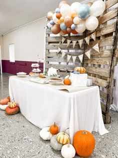 a table topped with lots of white and orange pumpkins next to a wooden wall