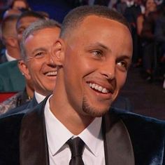 a man in a suit and tie smiling at the camera with other people behind him