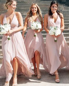 three bridesmaids in pink dresses walking down the stairs at their wedding ceremony with white bouquets