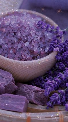 a wooden bowl filled with purple crystals next to lavender flowers and a spoon full of sugar cubes