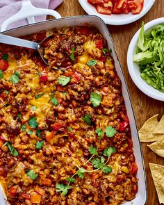 a casserole dish filled with mexican food and tortilla chips on the side