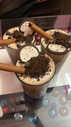 three cups filled with ice cream and cinnamons on top of a glass table next to candy