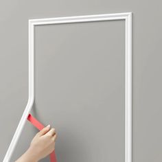 a hand holding a red piece of tape near a white frame on a gray wall