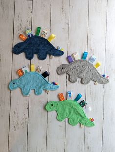 three felt dinosaurs are hanging on a white wooden wall with toothbrushes and toothpaste