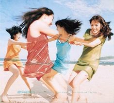 three girls are running on the beach with their arms around each other and one girl has her hair in the air