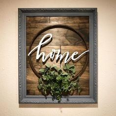 a wooden sign that says home with some greenery in front of it on a wall