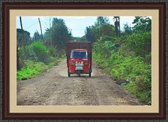 an old red truck driving down a dirt road