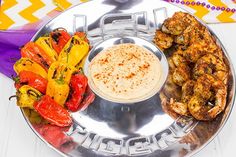 a silver plate topped with chicken and veggies next to a bowl of dip