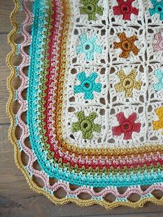 a crocheted granny blanket with multicolored flowers on it sitting on a wooden floor