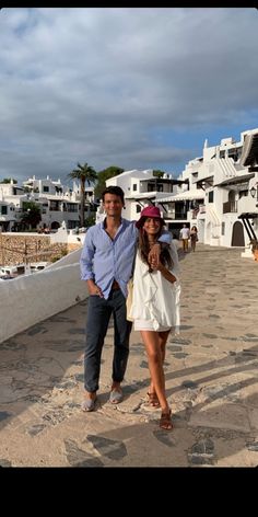 a man and woman posing for a photo in front of some white buildings with palm trees