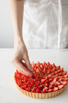 a person placing strawberries on top of a tart shell to make a strawberry tart