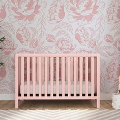 a pink crib in front of a floral wallpaper