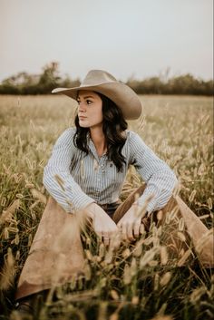 a woman wearing a cowboy hat sitting in a field