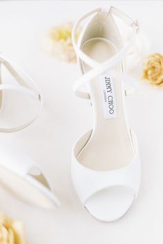 a pair of white high heeled shoes next to a bouquet of flowers on a white surface