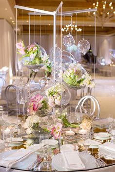 the table is set with clear vases, plates and flowers on it's centerpiece